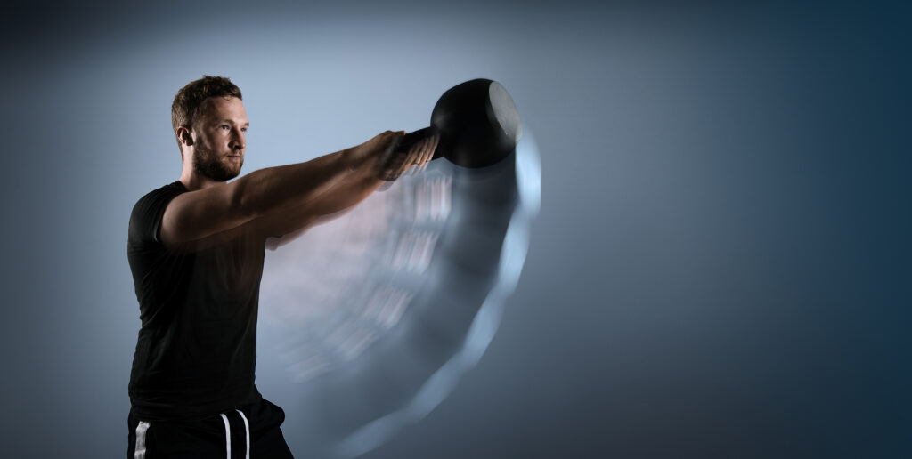 Ein Mann schwingt eine Kettlebell mit beiden Händen nach vorne, um die vordere Schultermuskulatur zu trainieren.